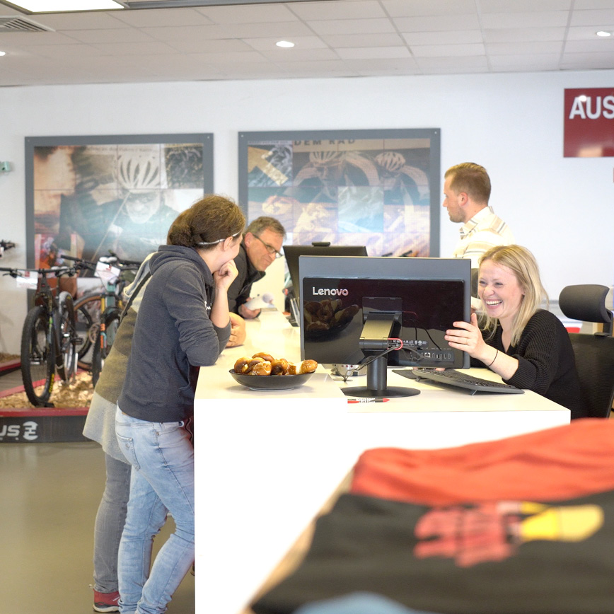 Lockerer Plausch an der Theke im Bike-Shop – Kund:innen und Team lachen gemeinsam, im Hintergrund stehen Bikes bereit.