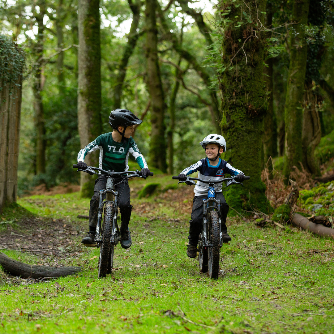 Zwei Kinder fahren fröhlich auf Mountainbikes durch einen moosbedeckten Wald.