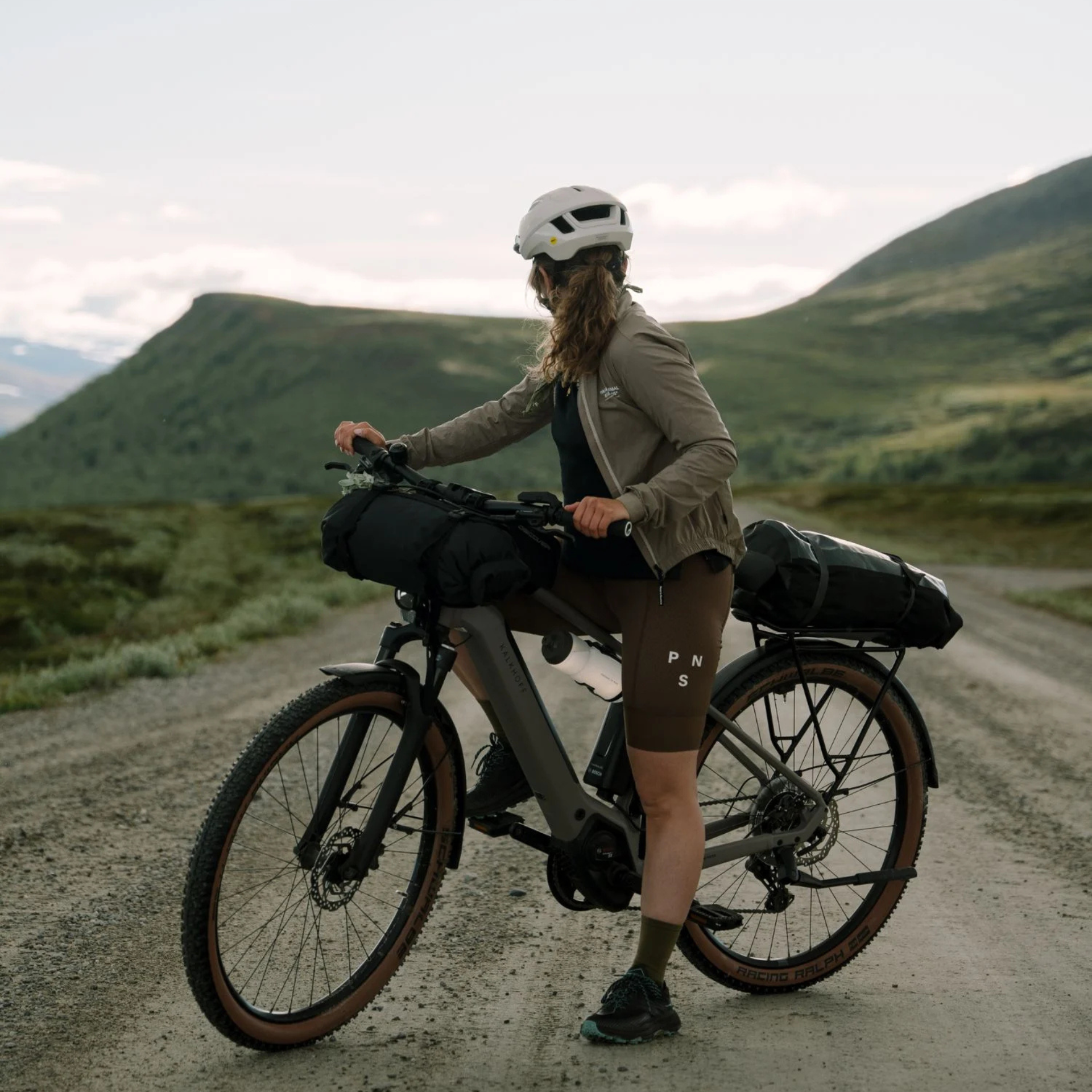 Frau mit Kalkhoff-Bike auf Schotterstraße in bergiger Landschaft.