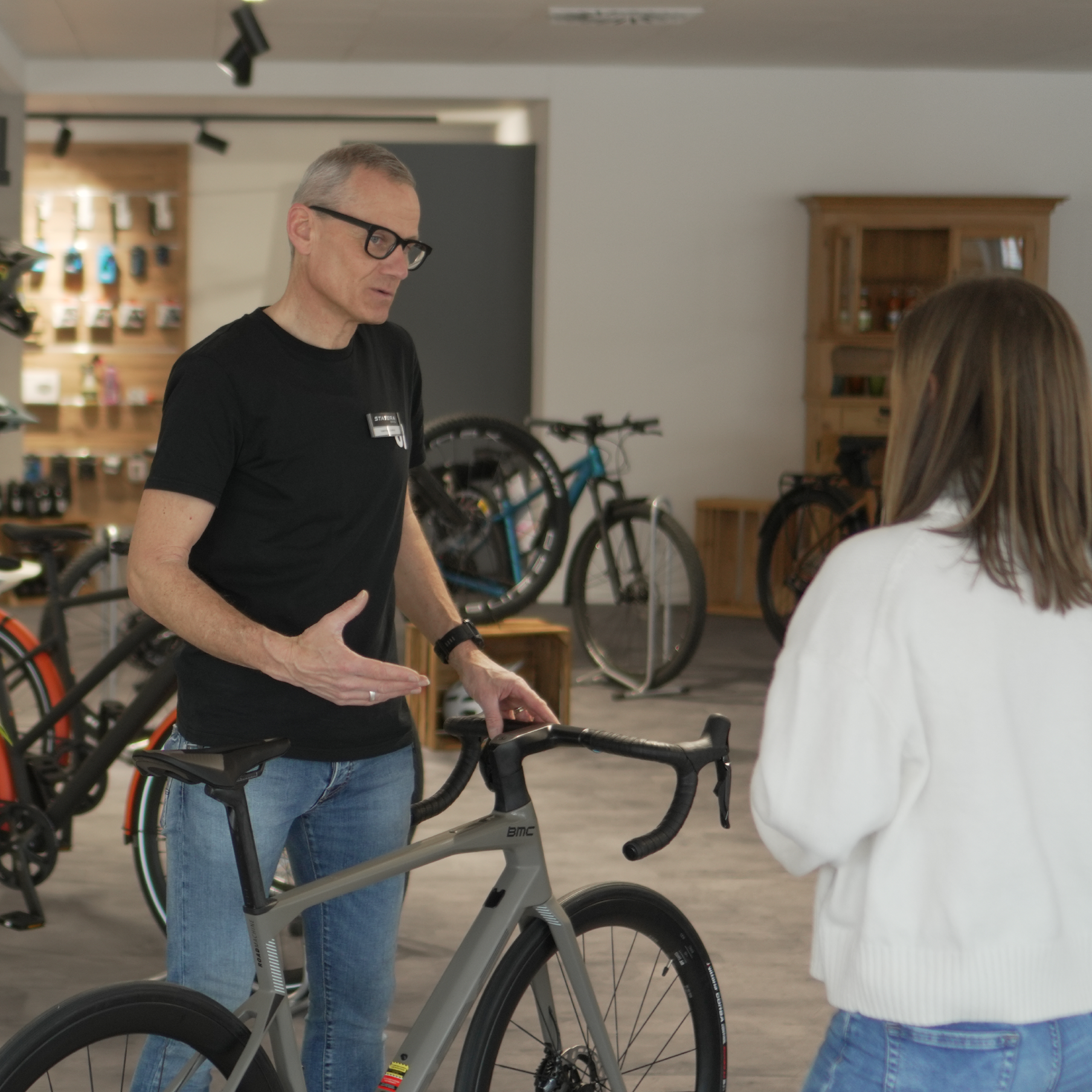 Verkäufer erklärt einer Kundin entspannt die Details eines Rennrads im modernen Fahrradladen – im Hintergrund stehen weitere Bikes.